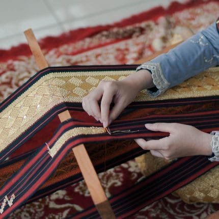 Jari jemari wanita sedang menyulam kain tapis khas Lampung dengan benang emas secara detail dan telaten