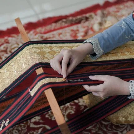 Jari jemari wanita sedang menyulam kain tapis khas Lampung dengan benang emas secara detail dan telaten
