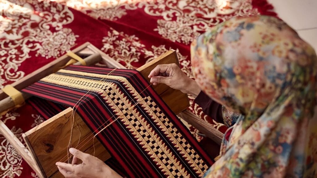 Foto pengrajin tapis sedang menapis kain tapis menggunakan alat peraga tradisional di workshop, menampilkan keahlian dan dedikasi dalam pembuatan produk berkualitas.