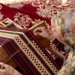Foto pengrajin tapis sedang menapis kain tapis menggunakan alat peraga tradisional di workshop, menampilkan keahlian dan dedikasi dalam pembuatan produk berkualitas.